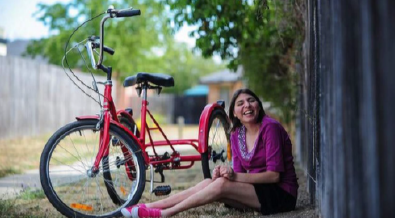 A woman sitting on the ground outside next to a red bike and a fence.