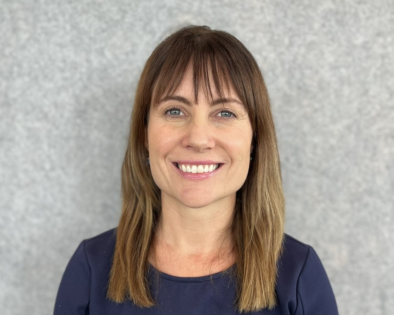 Portrait of Jennifer against a grey background, smiling at the camera.